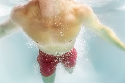 An image of a man diving in the pool with lots of air bubbles