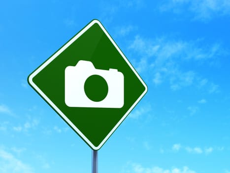 Vacation concept: Photo Camera on green road (highway) sign, clear blue sky background, 3d render