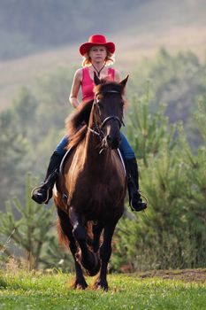 Woman in red hat galloping through the meadow on horseback a Friesian horse breed
