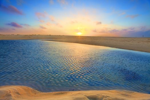 The summer sun rises over golden sand dunes and azure blue waters