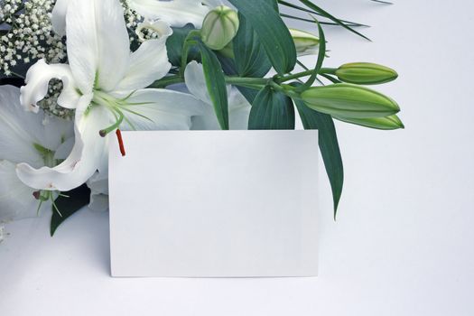 White lily flowers and post card over white background