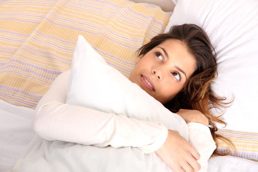 A daydreaming woman holding a pillow.