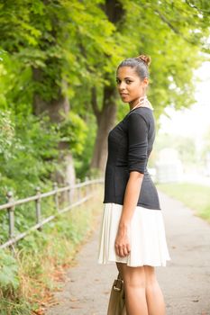 A young Girl walking in the park with her handbag.