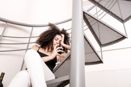 A young brazilian woman sitting on the stairs with a glass of red wine.