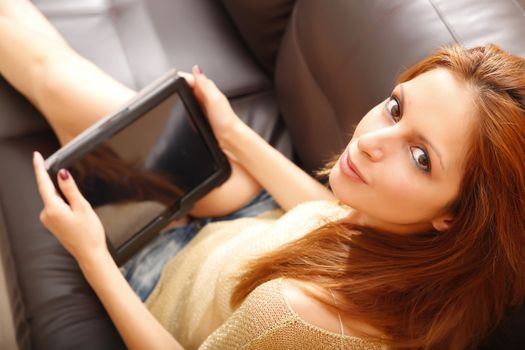 A young woman holding a Tablet PC while relaxing on the sofa.