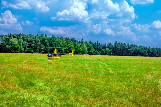 Yellow helicopter on green field by the woods
