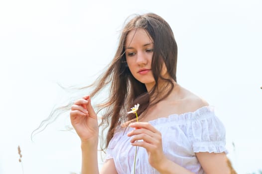 brunette girl with a camomile in a hand