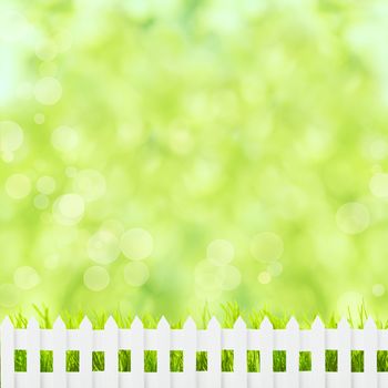 Green grass over spring bokeh and white fence