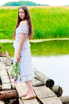 girl standing on the bridge over the river with a bouquet