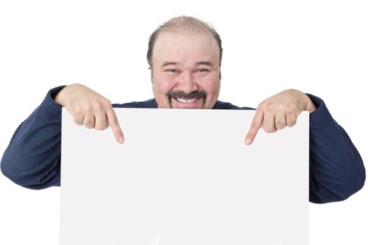 Motivated middle-aged businessman holding a blank white sign suitable for advertising or an announcement smiling happily and pointing to it with both hands to draw your attention to the information