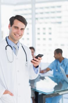 Doctor text messaging with group around table in background at hospital