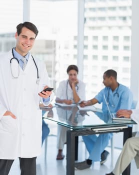 Doctor text messaging with group around table in background at hospital