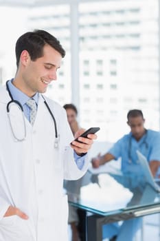 Doctor text messaging with group around table in background at hospital