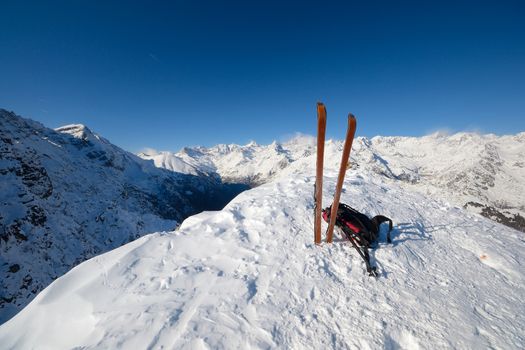 On the top of the mountain, pair of back country - tour ski and a backpack with avalanche safety tools. Scenic high mountain background (Gran Paradiso peak, 4061 m).