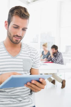 Smiling young man using digital tablet with colleagues in background at a creative bright office
