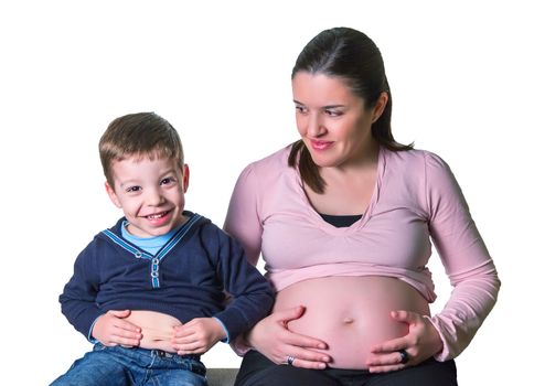 Pregnant mother and son laughing when comparing their bellies sitting on a sofa over white background