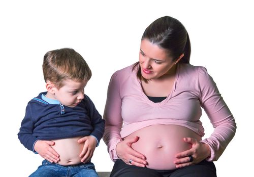 Pregnant mother and son laughing when comparing their bellies sitting on a sofa over white background