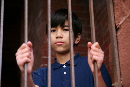 Boy standing behind bars, sad  or wary expression. Illustration purposes.