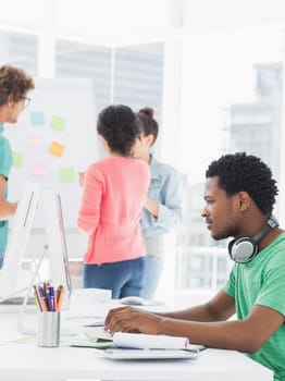 Side view of a casual man using computer with group of colleagues behind in a bright office