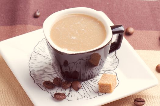 Cup of coffee with cube of brown sugar in a spoon close-up.