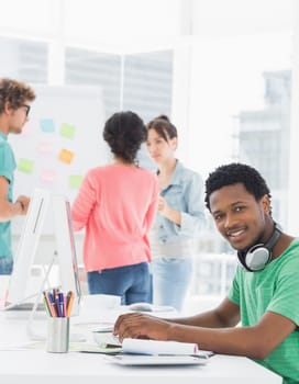 Side view portrait of a casual man using computer with group of colleagues behind in a bright office