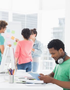 Side view of a casual man using digital tablet with group of colleagues behind in a bright office