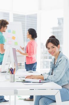 Side view portrait of a casual woman using computer with group of colleagues behind in a bright office