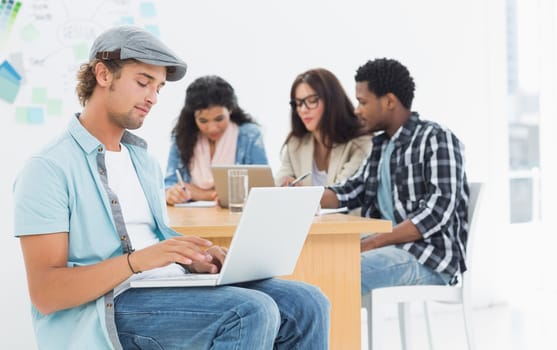 Concentrated casual man using laptop with group of colleagues behind in a bright office