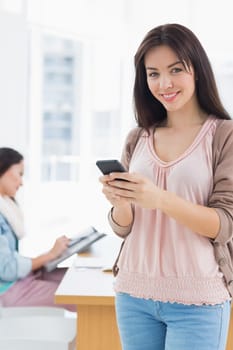 Portrait of a smiling casual young woman text messaging in a bright office