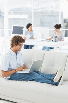 Young man using laptop with colleagues in background at a creative bright office