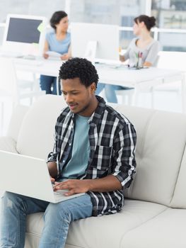 Young man using laptop with colleagues in background at a creative bright office