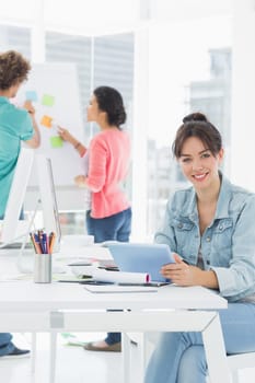 Portrait of a casual woman using digital tablet with group of colleagues behind in a bright office