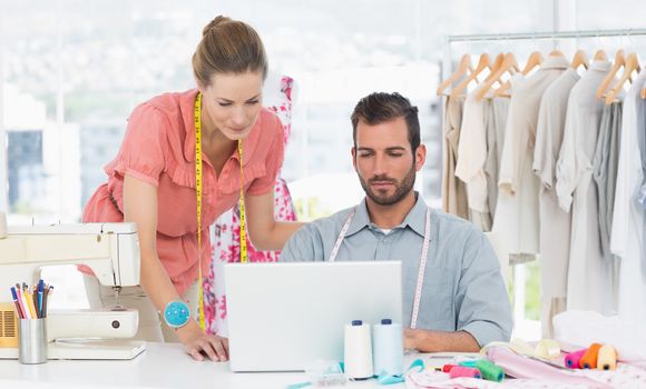 Male and female fashion designers using laptop at work in a bright studio