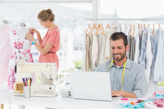 Young man using laptop with female fashion designer working in background at the studio