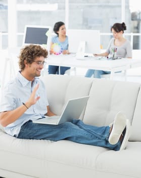 Young man using laptop with colleagues in background at a creative bright office