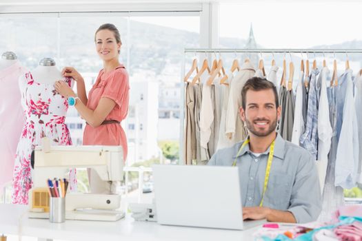 Young man using laptop with female fashion designer working in background at the studio