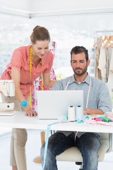 Male and female fashion designers using laptop in a bright studio
