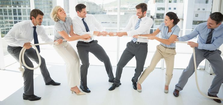 Full length of a group of business people playing tug of war in office