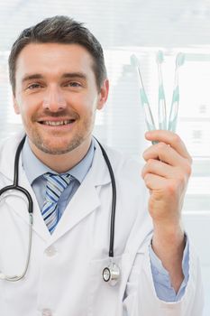 Portrait of a smiling doctor holding toothbrushes in his office