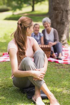 Portrait of a smiling woman with grandmother and granddaughter in background at the park
