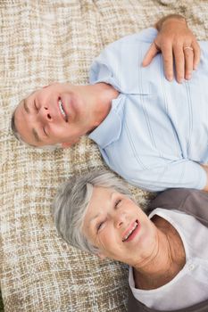 High angle view of a smiling relaxed senior couple lying in the park