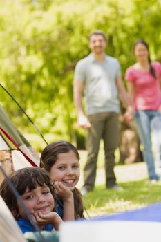 Portrait of kids in tent with blurred couple in background at park