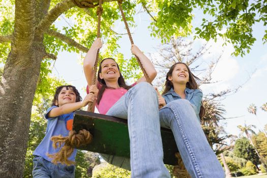 Low angle view of kids pushing mother on swing in playground