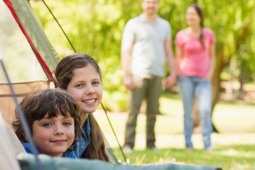 Portrait of kids in tent with blurred couple in background at park