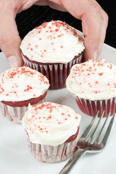 Close-up of a man's hand picking the biggest red velvet cupcake on the plate.