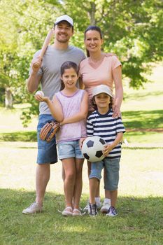 Full length portrait a family of four holding baseball bat and ball in the park