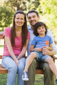 Portrait of a smiling couple with son sitting on park bench