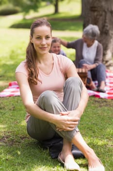 Portrait of a smiling woman with grandmother and granddaughter in background at the park