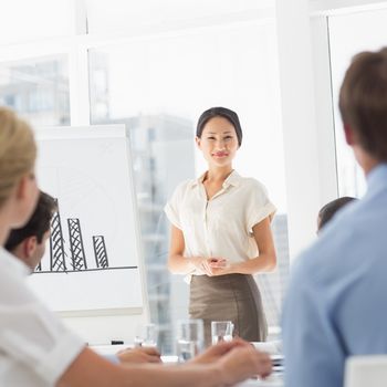 Pleased asian businesswoman presenting bar chart to colleagues in the office