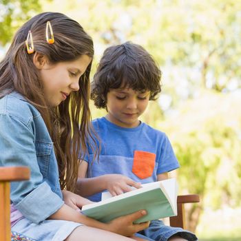 Side view of a young boy and girl reading book on park bench